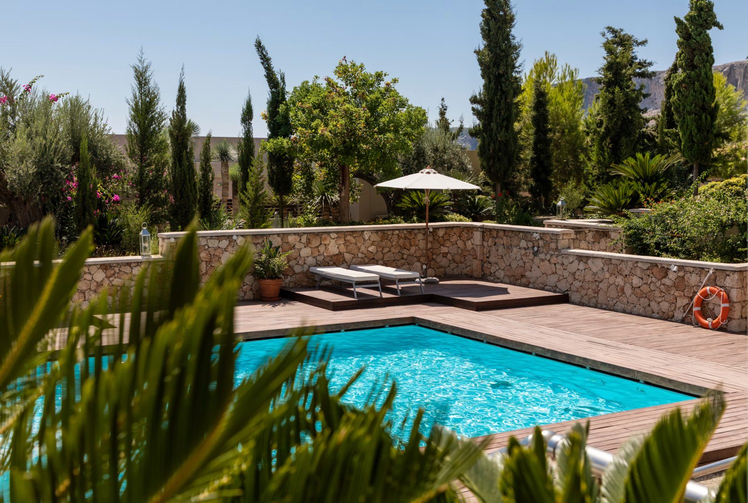 Piscina en un jardín mediterráneo con muro de piedra, tarima y tumbonas