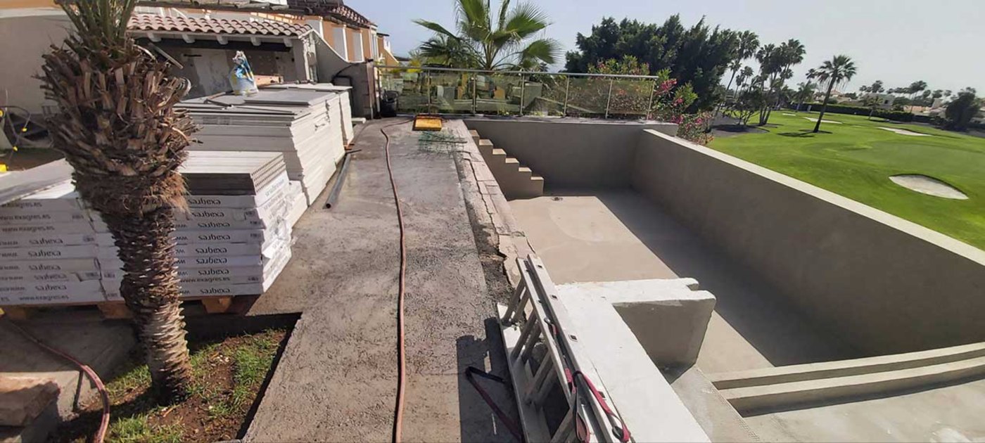 Vaso de piscina recién excavado y encofrado junto a un campo de golf, con el material de obra preparado