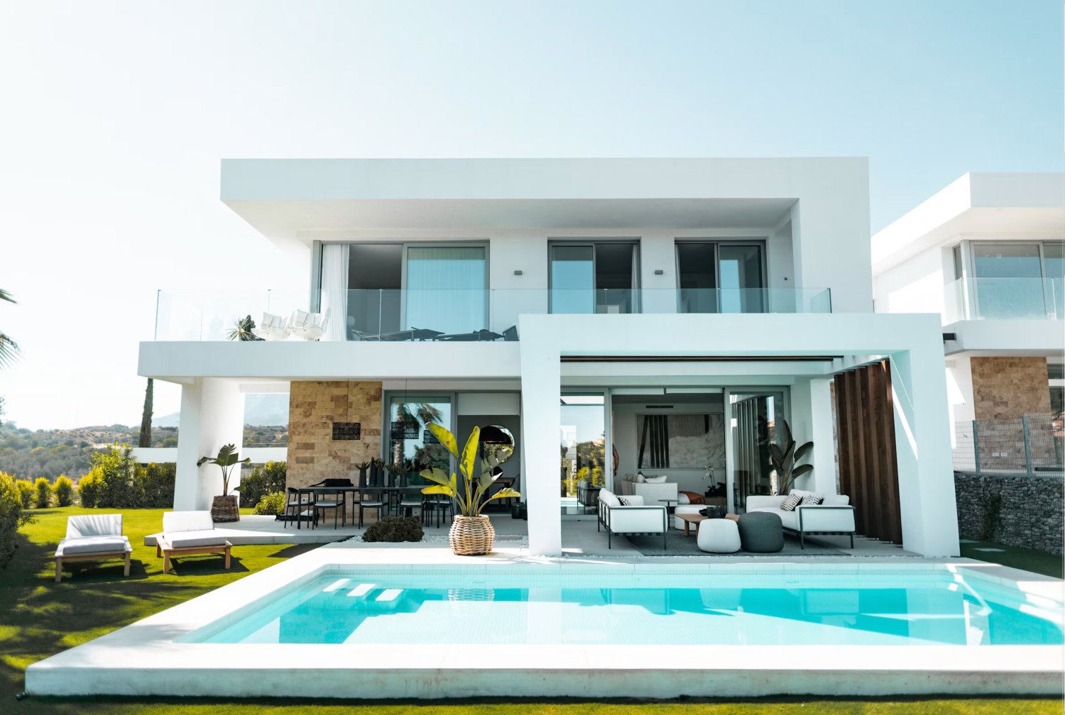 Villa blanca de dos plantas con piscina de hormigón de bordes rectos, terraza de piedra clara y jardín
